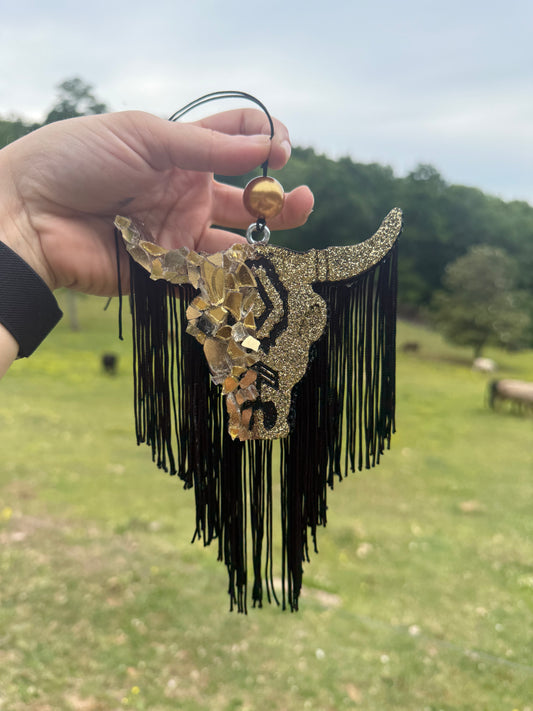 Hand holding a decorative cow skull with fringes against a blurred outdoor background